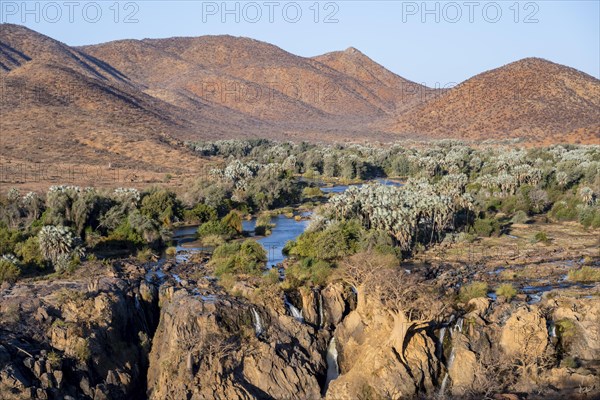 Kunene River with green vegetation in dry red mountain landscape, waterfall and African Baobab
