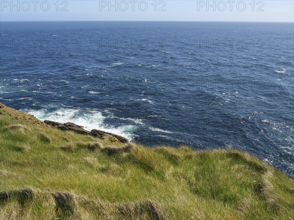 Peaceful coastline with views of the calm sea and grassy fields, green fields on the rugged