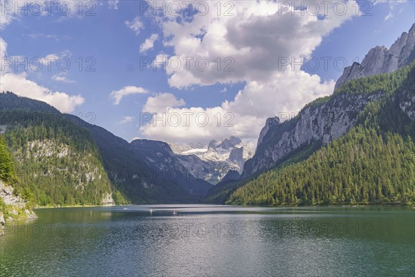 Picturesque lake surrounded by high mountains and forests under a cloudy sky, turquoise green