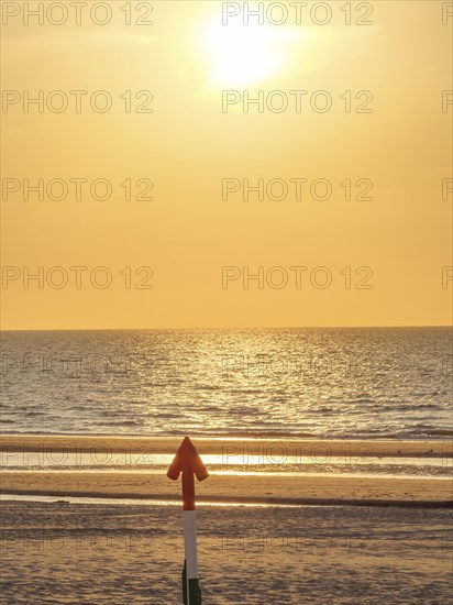 An arrow on the beach points towards the sea at sunset, the sky shines in golden light, sunset on
