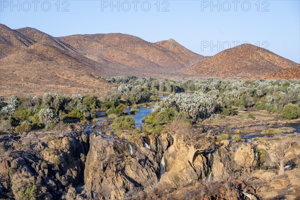 Kunene River with green vegetation in dry red mountain landscape, waterfall and African Baobab