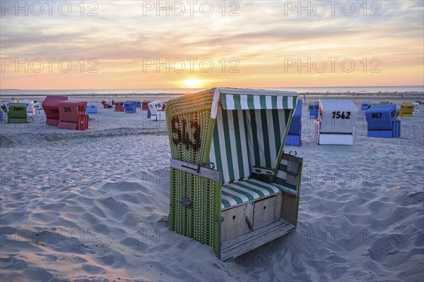 A green beach chair in a pit, surrounded by colourful beach chairs, at sunset, summer evening on