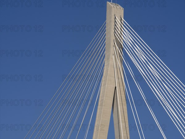 Part of a modern bridge with cable tensions under a clear blue sky, the old town of Dubrovnik with