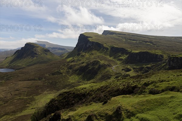 Quiraing, landscape in Scotland, view of rugged mountains and wide plains under a half-cloudy sky