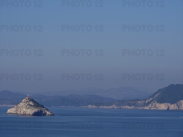 Small rocky island with lighthouse, surrounded by calm waters and mountains in the background, the