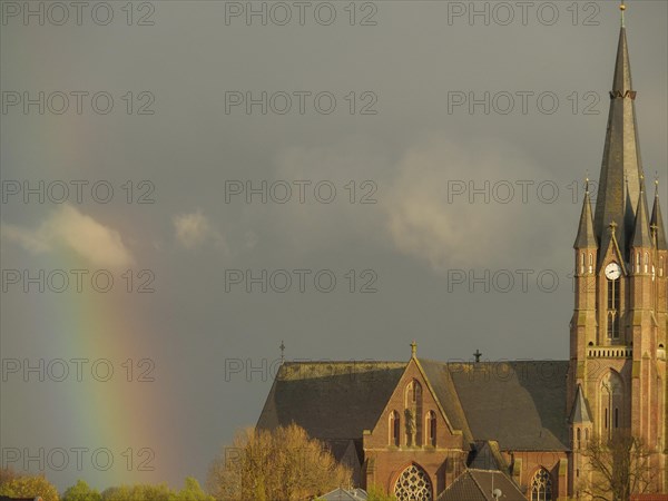A gothic church with a high tower under a cloudy sky and a rainbow in the background, rainbow at a