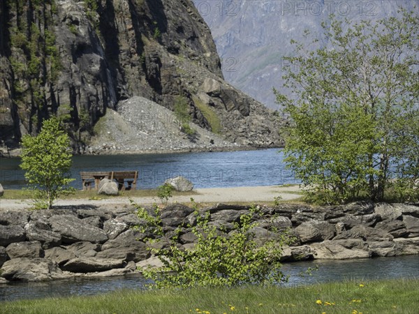 Cosy lake with mountains in the background, trees and a bench on the shore, spring in the fjord