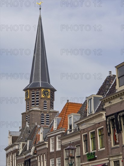 Church tower with clock and surrounding historic buildings under a blue sky, historic houses in