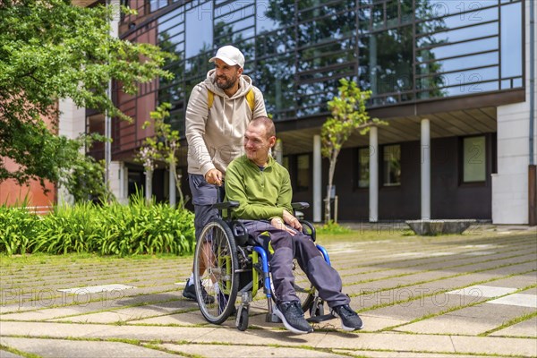 University student pushing the wheelchair of a disabled friend outdoors in the university campus
