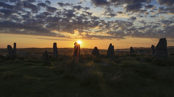 Stone circle at sunset with bright sunlight and clouds in the sky, Isle of Lewis & Harris