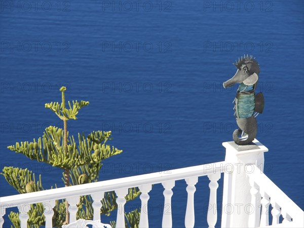 Seahorse sculpture on a railing in front of a deep blue sea and blue sky in Greece, The volcanic