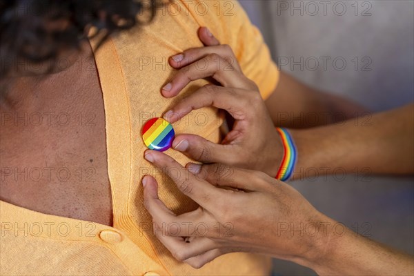 Close-up of gay man pinning a LGBT badge on his couple sitting on the sofa