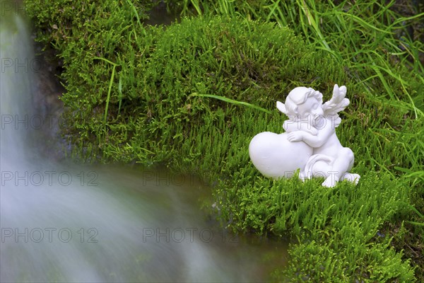 Porcelain angel figurine on moss by a waterfall