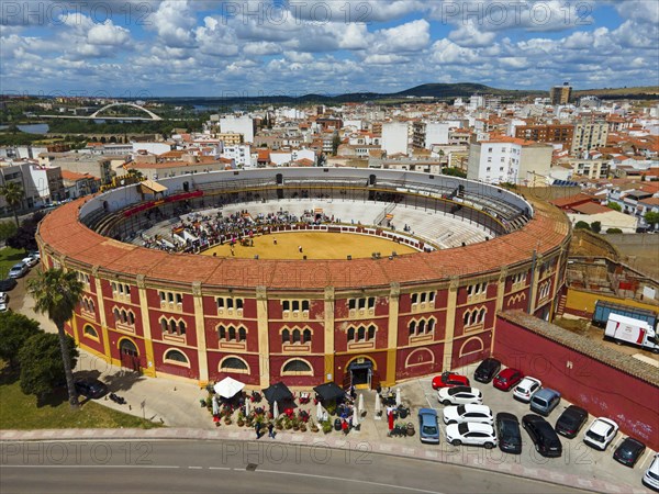 Bullring with red and yellow accents in the middle of a city under a cloudy sky, with parked cars