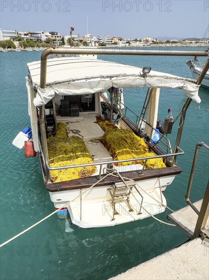 Fishing boat moored to quay wall in Kokkinos Pyrgos harbour, yellow fishing nets on board, Kokkinos