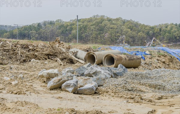 Old dirty concrete culvert sections on ground beside tree branches at construction site in Daejeon,