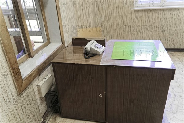 Abandoned, old-fashioned desk with telephone. Illuminated window and wooden panelling on the walls,