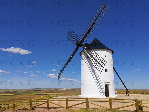 A windmill stands alone in a field under a bright blue sky in a vast summer landscape, aerial view,