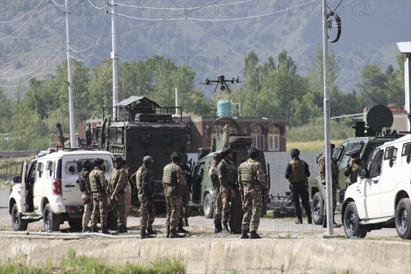 Military personnel standing near vehicles with equipment, conducting an operation in a mountainous