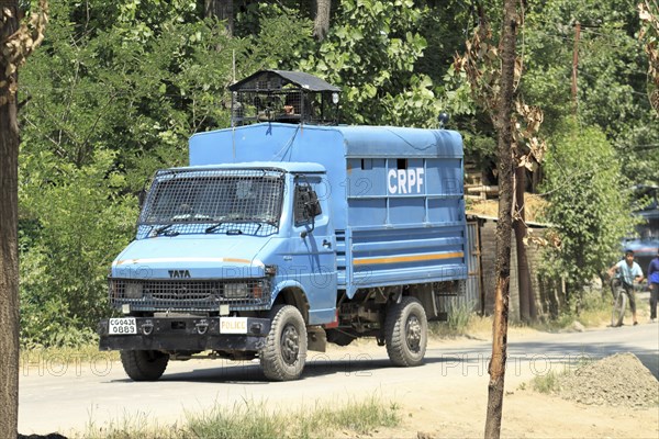 Blue police truck patrolling along a road lined with trees on a sunny day, Encounter, Pulwama,