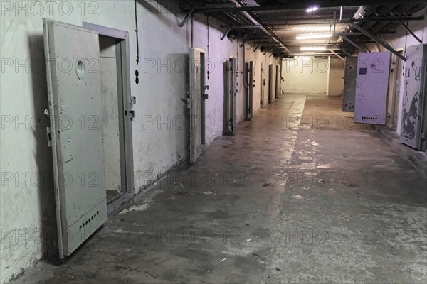 Long prison corridor with several open metal cell doors. Gloomy and deserted atmosphere,