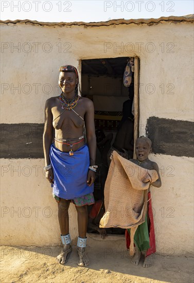 Hakaona woman with traditional kapapo hairstyle and colourful necklaces, with child, in front of