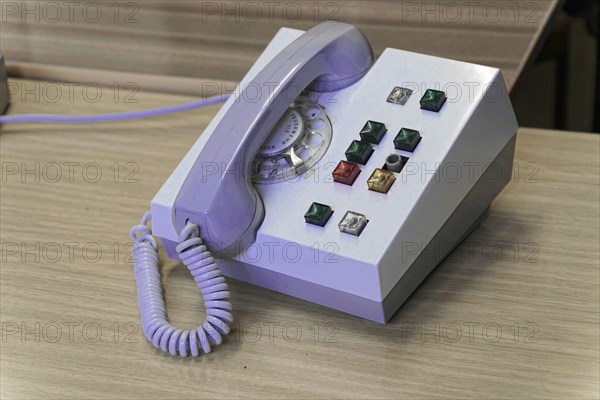 Close-up of an old rotary-disc telephone with various control buttons on a wooden desk,