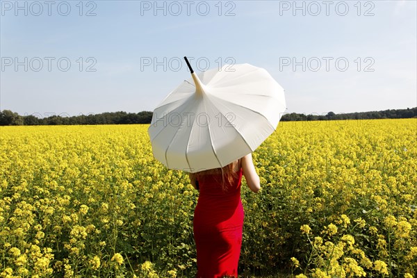 Woman standing in a rape field with a white parasol