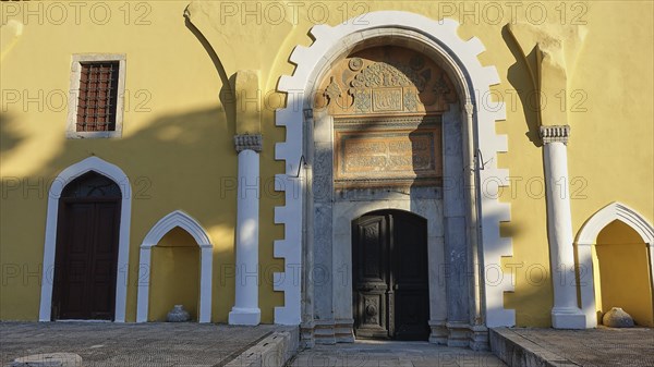 Ottoman Library, Yellow historical facade of a building with an ornate entrance arch, inscriptions