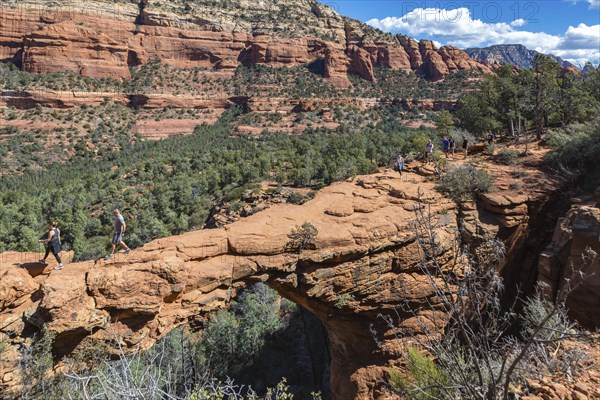 Hikers cross the Devil's Bridge natural arch along the Devil's Bridge Trail in Sedona, Arizona,