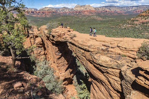 Hikers cross the Devil's Bridge natural arch along the Devil's Bridge Trail in Sedona, Arizona,