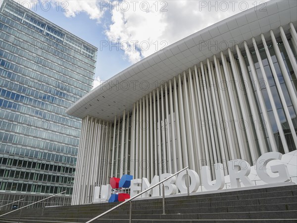 Modern building in Luxembourg with glass facade and striking columns next to a skyscraper, under a