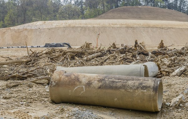 Old dirty concrete culvert sections on ground in front of tree branches at construction site in