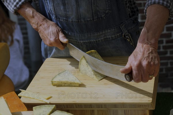 A man in traditional clothing cuts cheese into slices for tasting at the Alkmaar cheese market.,