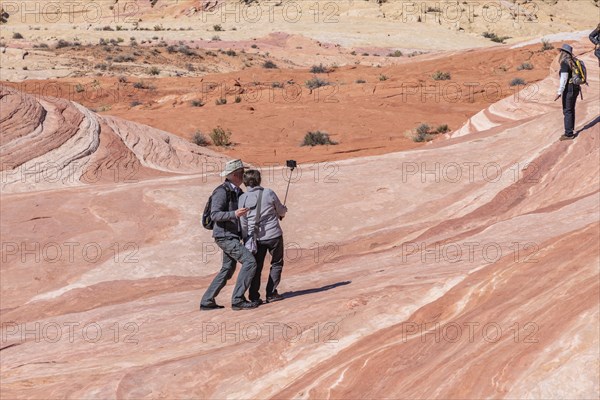 Couple use selfy stick for picture on a layered sandstone rock formation in the Fire Wave area of