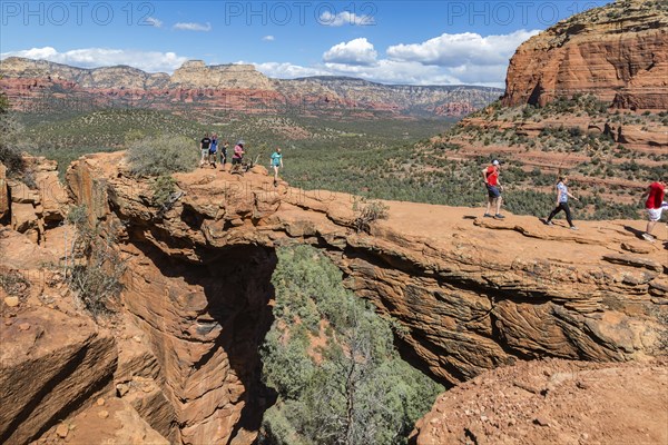 Hikers cross the Devil's Bridge natural arch along the Devil's Bridge Trail in Sedona, Arizona,