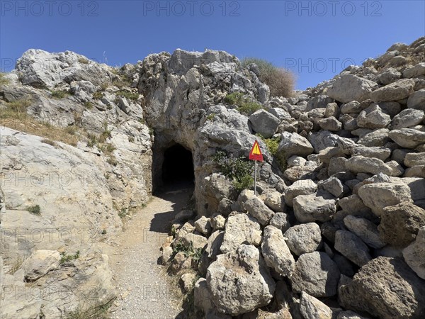 Entrance of a developed cave next to a warning sign warning of falling rocks on the site of the