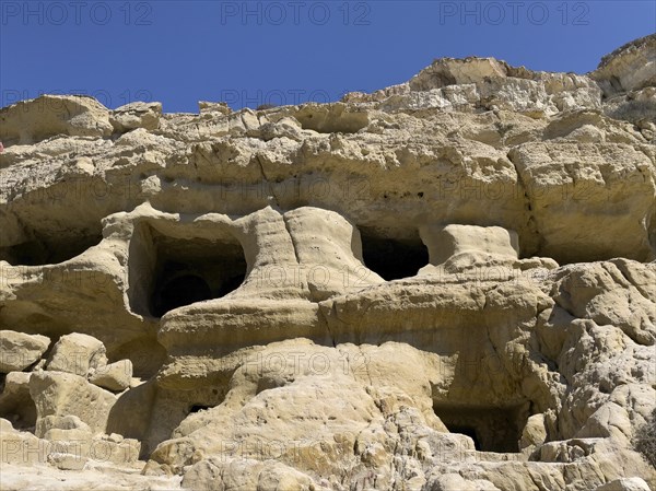View upwards to sandstone rocks at the edge of Matala bay with entrances to caves of former Roman