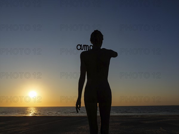 A silhouetted figure in front of a sunset on the beach, sunset in many colours on the beach with a