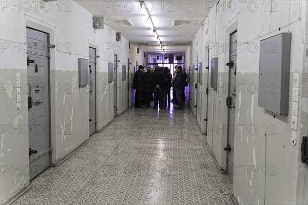 Group of people in the corridor of a prison with grey doors and neon lighting,