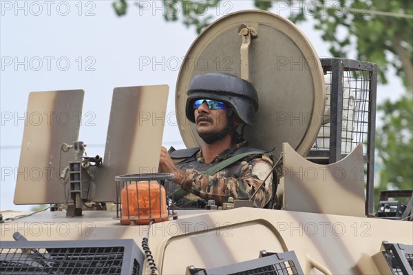 A soldier in an armored vehicle wearing a helmet and sunglasses, leaving encounter site in Pulwama,