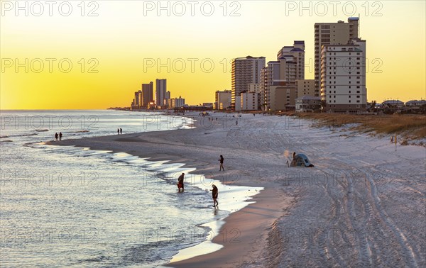 People walking and playing on the beach as the sun sets over the Gulf of Mexico at Gulf Shores,