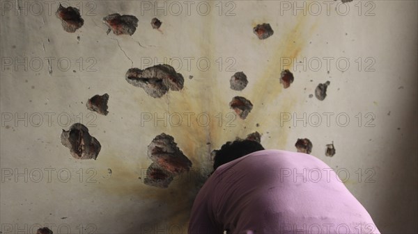 A man facing a wall riddled with bullet holes, sign of destruction in an indoor setting, Encounter,