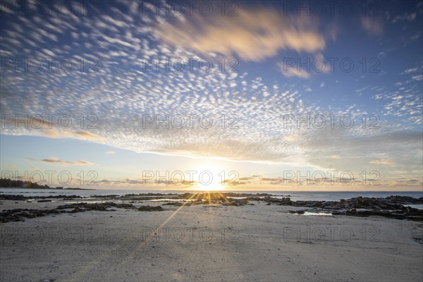 Sunrise over the sea with gentle waves. Sandy beach with lava rocks and blue water alternating with