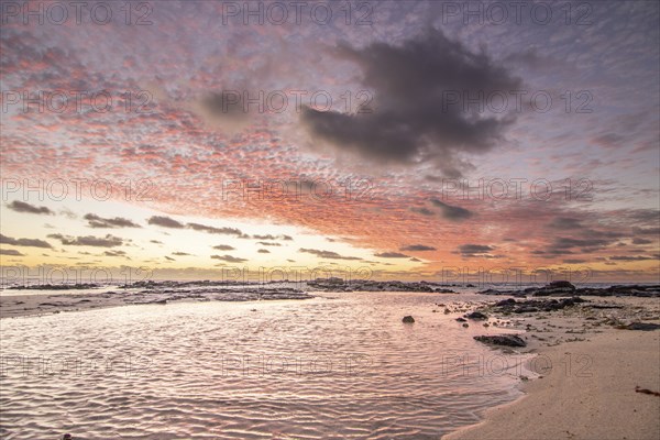 Sunrise over the sea with gentle waves. Sandy beach with lava rocks and blue water alternating with