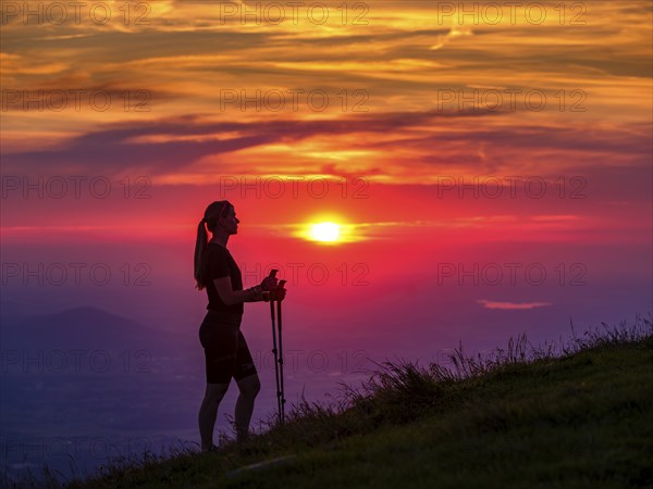 Silhouette of a young slender woman with hiking poles on a mountain meadow at sunset, Schlenken,