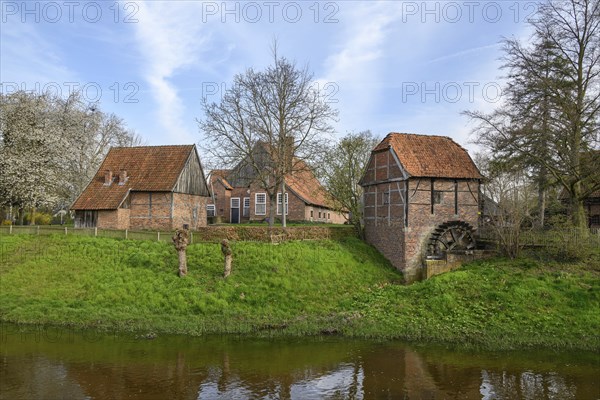 Small historic village with farmhouses, windmill and a river with a water wheel in a rural