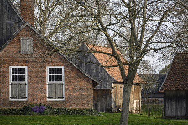 Old brick farmhouse with wooden doors and windows, surrounded by trees and a rural setting, Vreden,