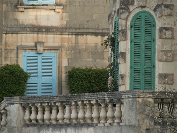 Close-up view of a building with green shutters, balcony railings and landscaped garden, valetta,