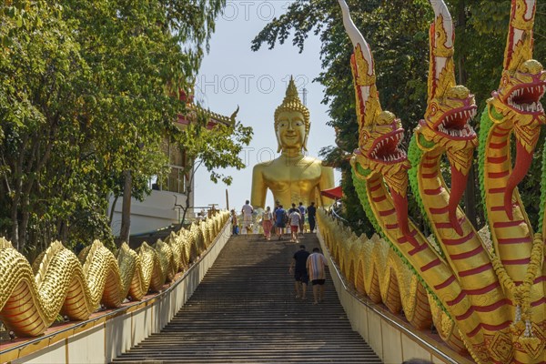 Large golden Buddha statue at the end of a staircase, flanked by dragon statues and visited by